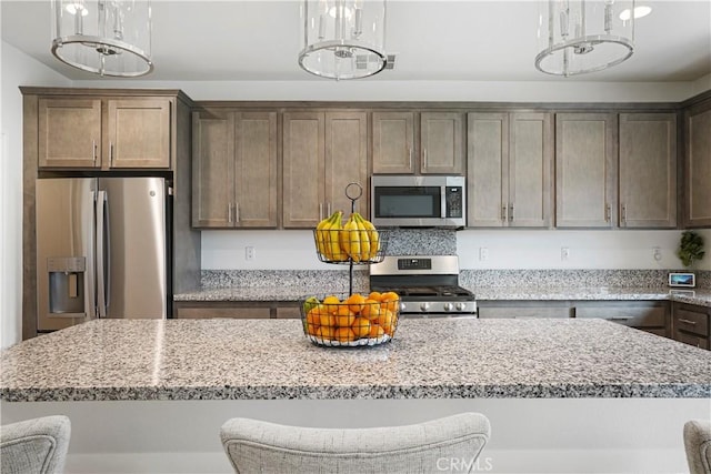 kitchen with a kitchen island, decorative light fixtures, appliances with stainless steel finishes, light stone counters, and a notable chandelier
