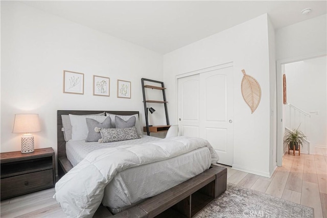 bedroom with baseboards, light wood-type flooring, and a closet