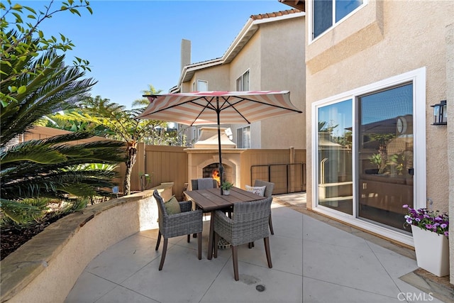 view of patio / terrace featuring outdoor dining area, a warm lit fireplace, and fence