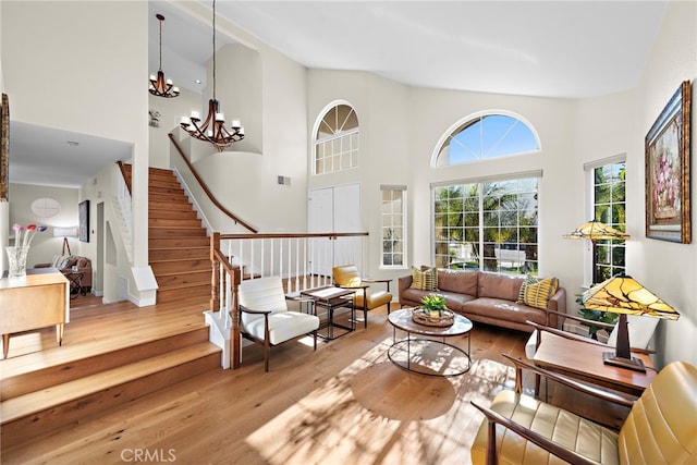 living room featuring wood finished floors, a towering ceiling, stairs, and an inviting chandelier