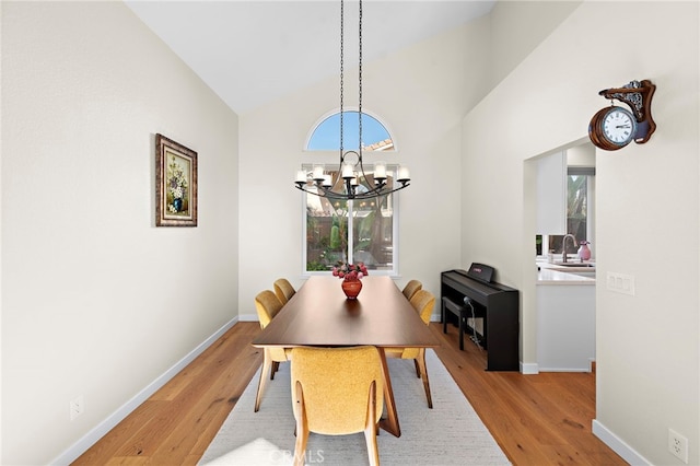 dining area with high vaulted ceiling, baseboards, a chandelier, and light wood-style flooring