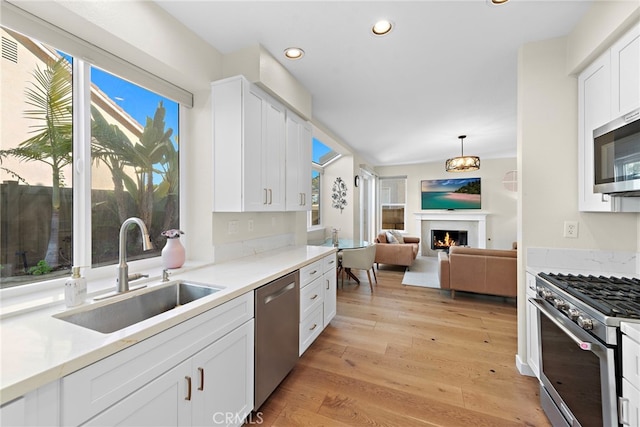 kitchen with a sink, a warm lit fireplace, white cabinets, appliances with stainless steel finishes, and recessed lighting