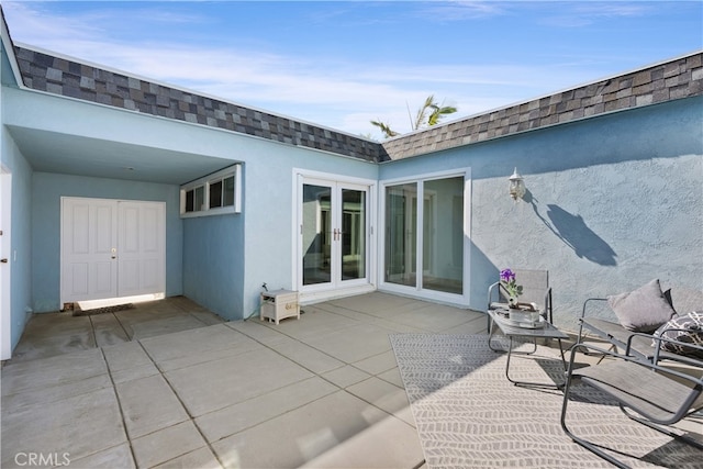 back of property with a shingled roof, mansard roof, stucco siding, french doors, and a patio