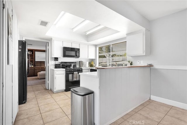 kitchen with light tile patterned floors, light countertops, black appliances, a peninsula, and white cabinetry