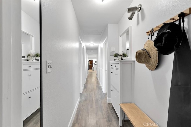 hallway with light wood-type flooring, attic access, and baseboards