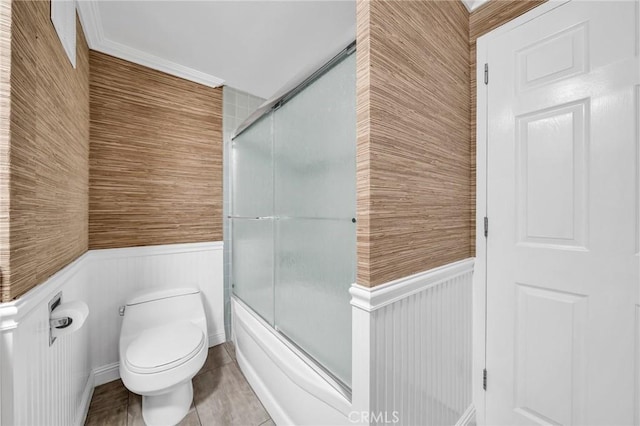 full bathroom featuring toilet, a wainscoted wall, and bath / shower combo with glass door