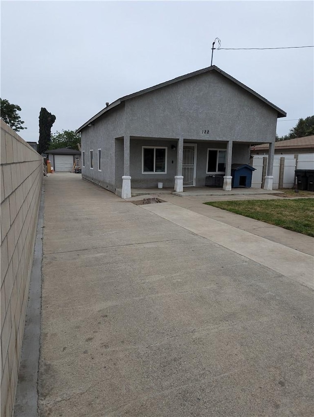 exterior space featuring stucco siding, an outdoor structure, fence, and covered porch
