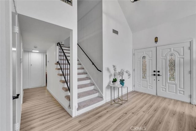 entrance foyer with high vaulted ceiling, wood finished floors, stairs, baseboards, and visible vents