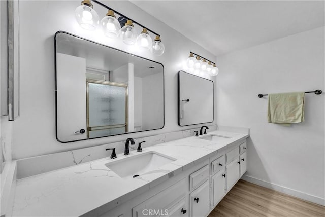 full bath with double vanity, wood finished floors, a shower with door, and a sink