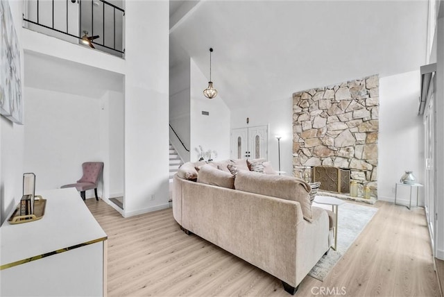 living area with baseboards, light wood-type flooring, stairs, and high vaulted ceiling