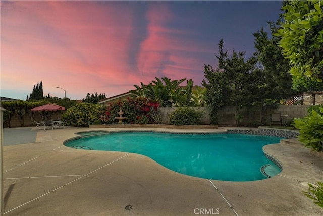 pool at dusk featuring a fenced backyard, a patio, and a fenced in pool