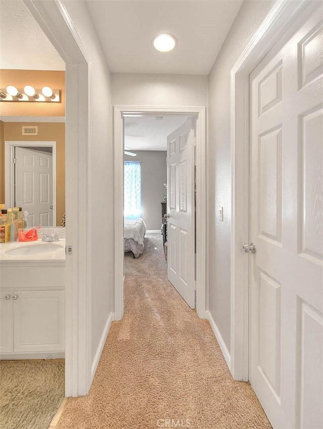 hallway with light carpet, a sink, and baseboards