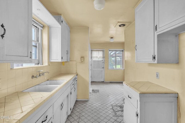 kitchen featuring a sink, baseboards, backsplash, white cabinetry, and tile counters