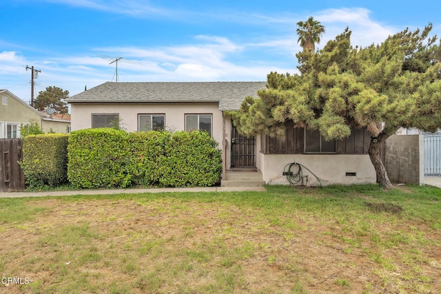 bungalow with stucco siding, a shingled roof, a front lawn, and fence
