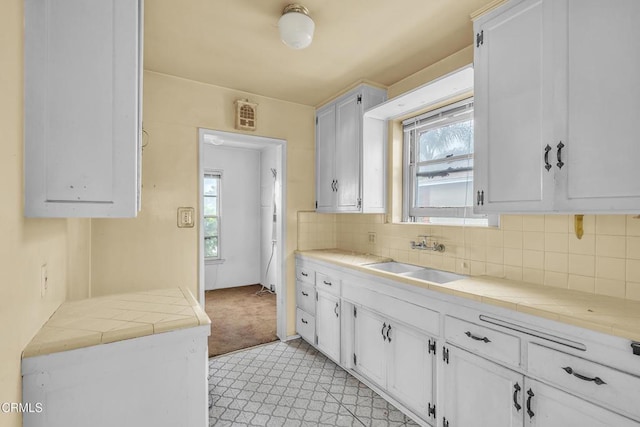 kitchen featuring tile countertops, white cabinetry, tasteful backsplash, and a sink