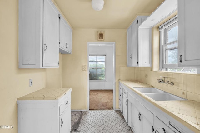 kitchen featuring white cabinets, decorative backsplash, a sink, and tile countertops