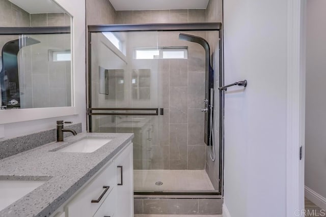 full bath with baseboards, a sink, double vanity, and a stall shower
