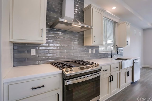 kitchen with a sink, decorative backsplash, stainless steel gas range, wall chimney exhaust hood, and dark wood-style floors