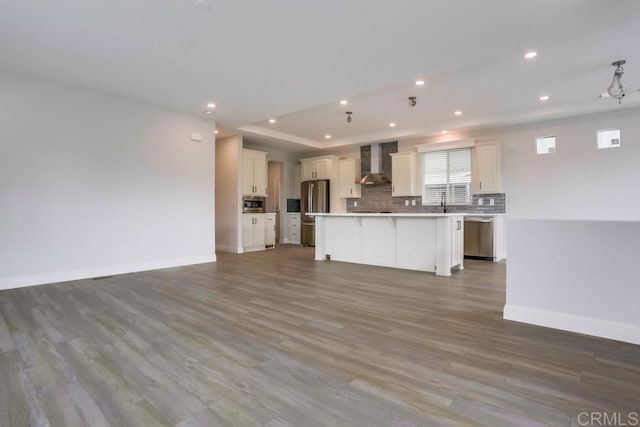 kitchen with open floor plan, wall chimney exhaust hood, appliances with stainless steel finishes, a kitchen island, and recessed lighting