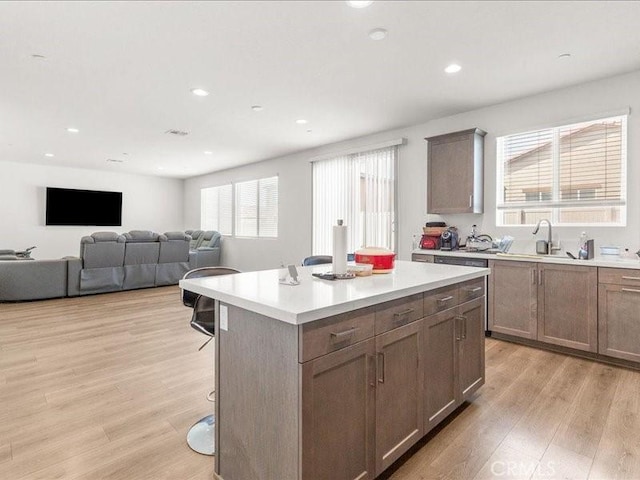 kitchen featuring a center island, a kitchen breakfast bar, a sink, light wood-style flooring, and light countertops