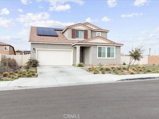 traditional home featuring driveway, a tiled roof, fence, stucco siding, and solar panels