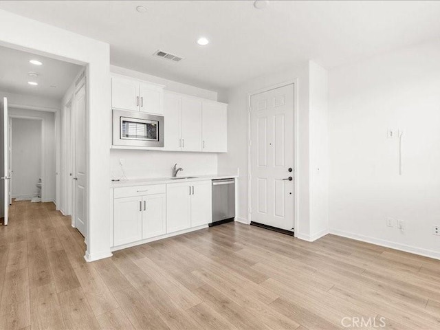 kitchen with a sink, light countertops, light wood-style flooring, appliances with stainless steel finishes, and visible vents