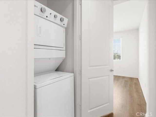 washroom with light wood-type flooring, stacked washer and dryer, and laundry area
