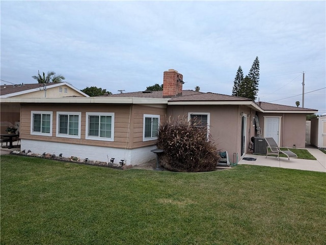 back of house with central AC, a chimney, a patio area, a lawn, and stucco siding