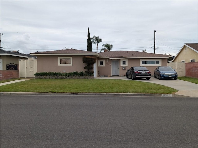 ranch-style house featuring concrete driveway, a front lawn, stucco siding, and fence