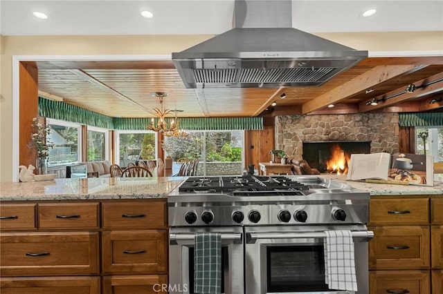 693 Old Meadow Pl, Lake Arrowhead, CA 92352 - kitchen with wall chimney range hood, a fireplace, brown cabinets, and double oven range