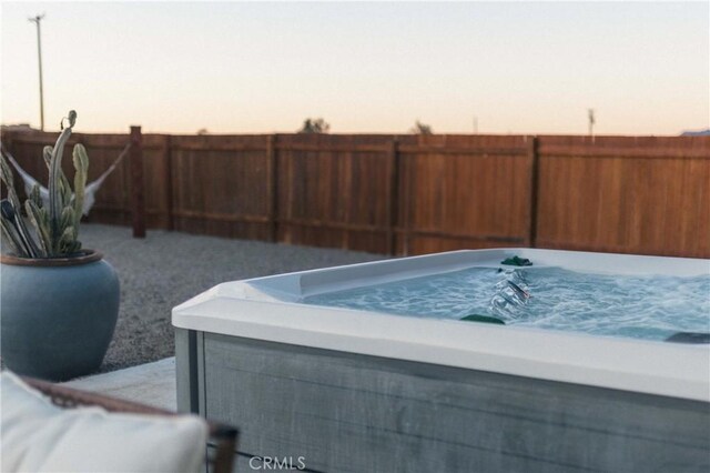 patio terrace at dusk featuring a fenced backyard and a hot tub