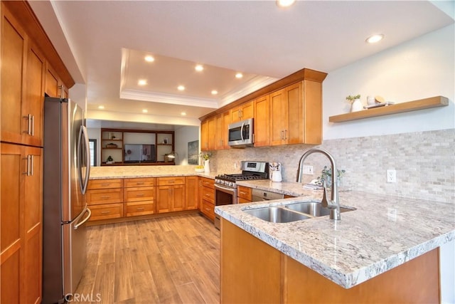 kitchen featuring brown cabinets, a sink, stainless steel appliances, a tray ceiling, and a peninsula