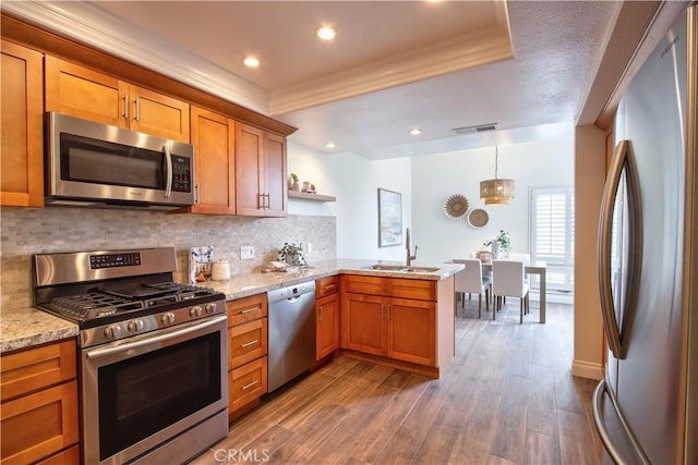 kitchen with stainless steel appliances, crown molding, a peninsula, and a sink
