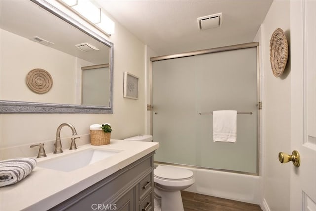 full bath with vanity, toilet, combined bath / shower with glass door, visible vents, and wood finished floors