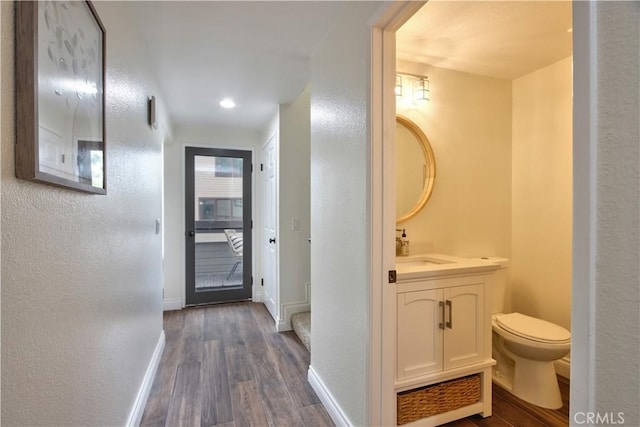 bathroom with wood finished floors, toilet, a textured wall, vanity, and baseboards