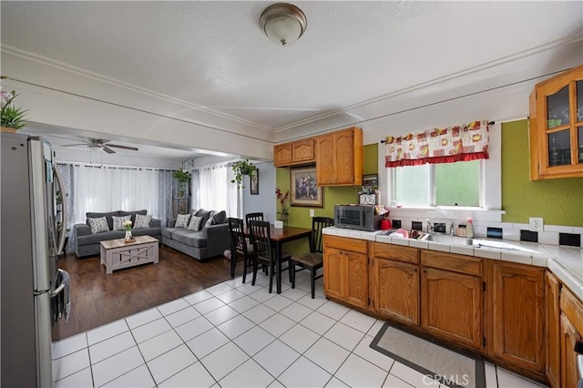 kitchen with open floor plan, glass insert cabinets, appliances with stainless steel finishes, crown molding, and light tile patterned floors