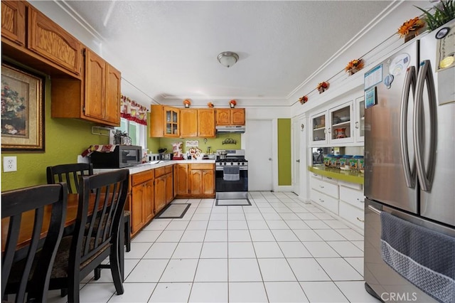 kitchen featuring brown cabinets, under cabinet range hood, light countertops, ornamental molding, and appliances with stainless steel finishes