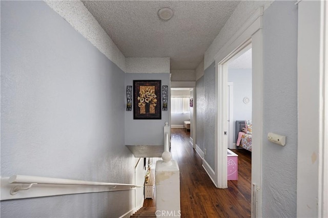 hallway featuring dark wood-type flooring, a textured wall, a textured ceiling, and baseboards