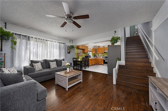 living area featuring light wood-style floors, a textured ceiling, a ceiling fan, and stairs