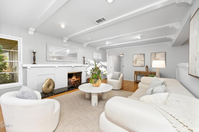 living area with visible vents, a fireplace, wood finished floors, and beam ceiling