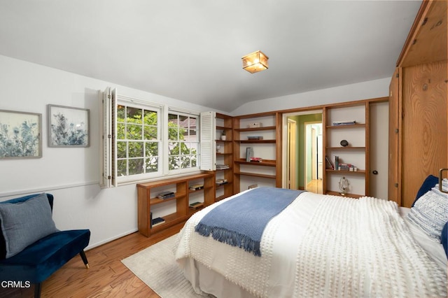 bedroom with vaulted ceiling, light wood-style floors, and baseboards