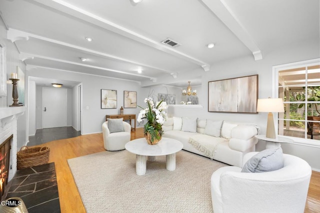living area with a fireplace with flush hearth, wood finished floors, visible vents, and beam ceiling