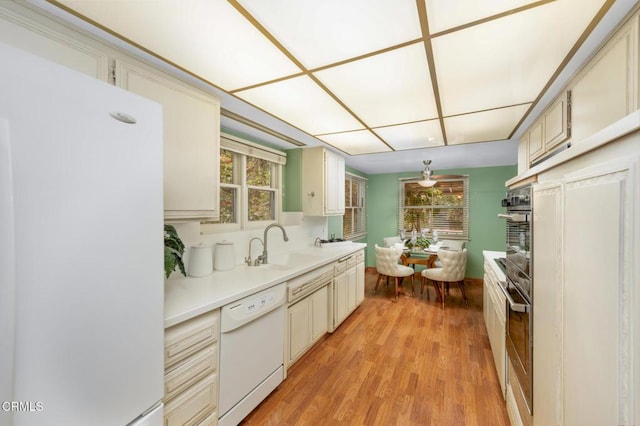 kitchen featuring a sink, white appliances, light countertops, a healthy amount of sunlight, and light wood-style flooring