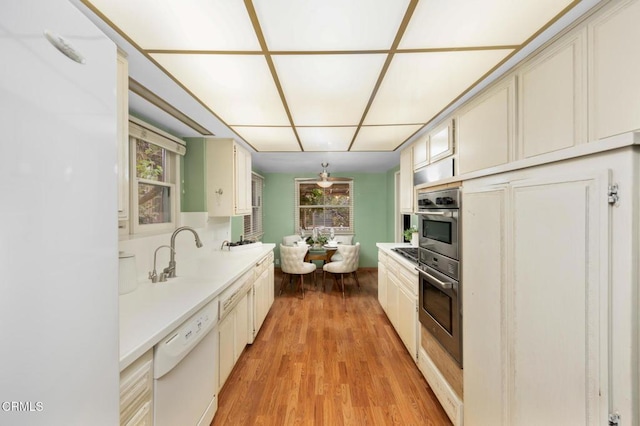 kitchen with dishwasher, a sink, light wood finished floors, and light countertops