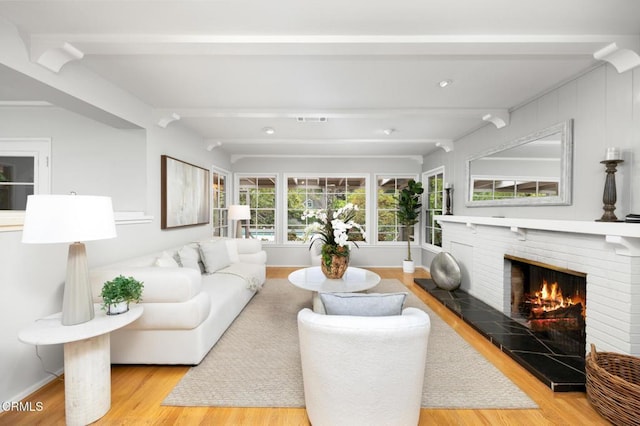living area featuring beamed ceiling, wood finished floors, visible vents, and a fireplace
