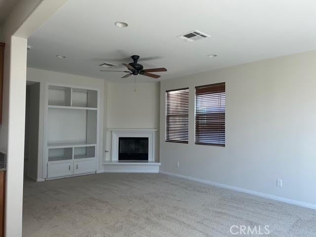 unfurnished living room with a ceiling fan, carpet, baseboards, a glass covered fireplace, and visible vents
