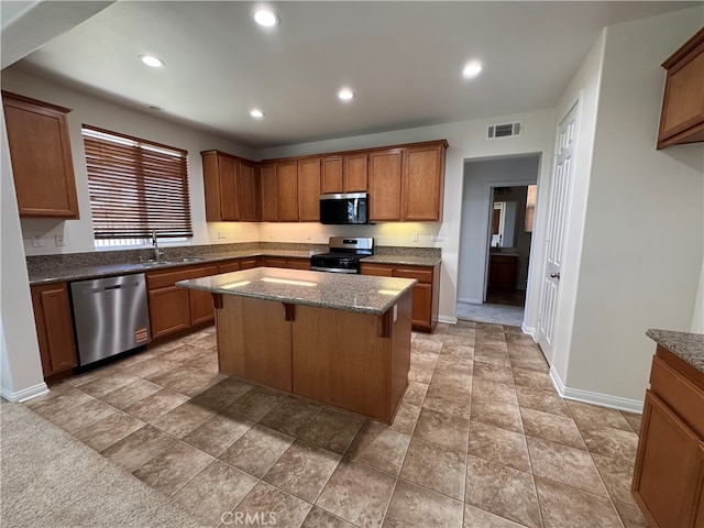 kitchen with dark stone countertops, brown cabinetry, visible vents, appliances with stainless steel finishes, and a kitchen island