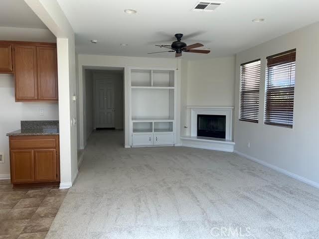 unfurnished living room featuring a ceiling fan, baseboards, visible vents, and a fireplace with raised hearth