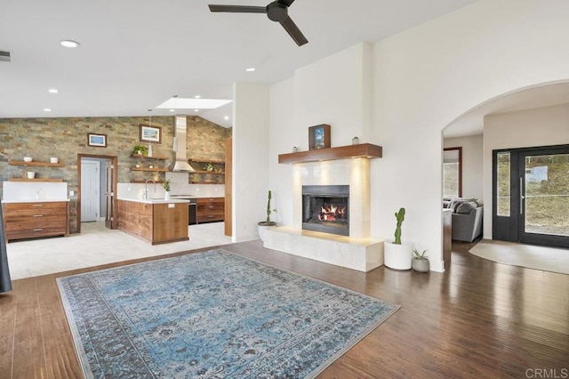 12502 Arboleda Vista Dr, Valley Center, CA 92082 - living area featuring arched walkways, light wood finished floors, ceiling fan, a glass covered fireplace, and high vaulted ceiling