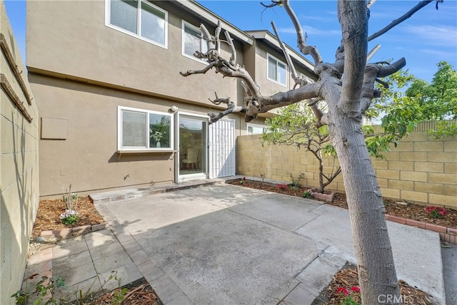 rear view of house featuring stucco siding, fence, and a patio area